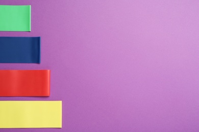 Set of fitness elastic bands on purple background, flat lay. Space for text Photo of Set of fitness elastic bands on purple background, flat lay. Space for text