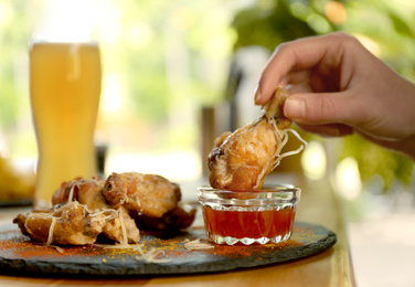 Woman dipping tasty BBQ wing into sauce at table, closeup Photo of Woman dipping tasty BBQ wing into sauce at table, closeup