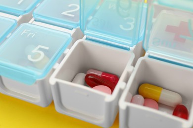 Plastic box with different pills on yellow background, closeup Photo of Plastic box with different pills on yellow background, closeup