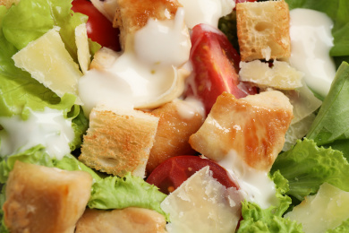 Tasty Caesar salad with chicken as background, closeup Photo of Tasty Caesar salad with chicken as background, closeup