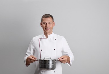 Happy male chef with cooking pot on light grey background Photo of Happy male chef with cooking pot on light grey background