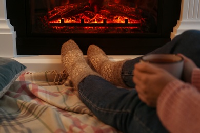 Woman in warm socks with cup of hot drink resting near fireplace at home, closeup Photo of Woman in warm socks with cup of hot drink resting near fireplace at home, closeup