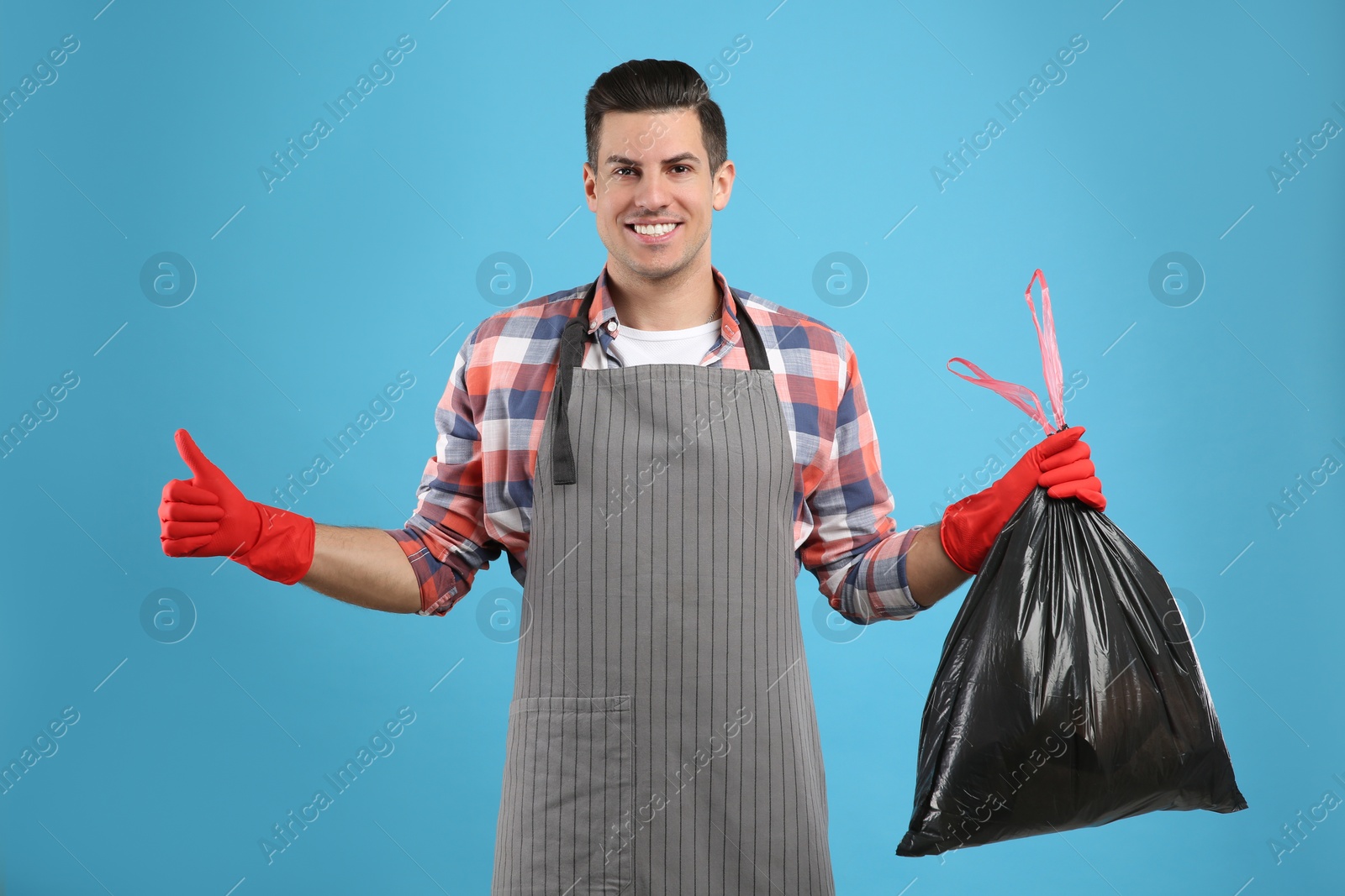 Man holding full garbage bag on light blue background Photo of Man holding full garbage bag on light blue background
