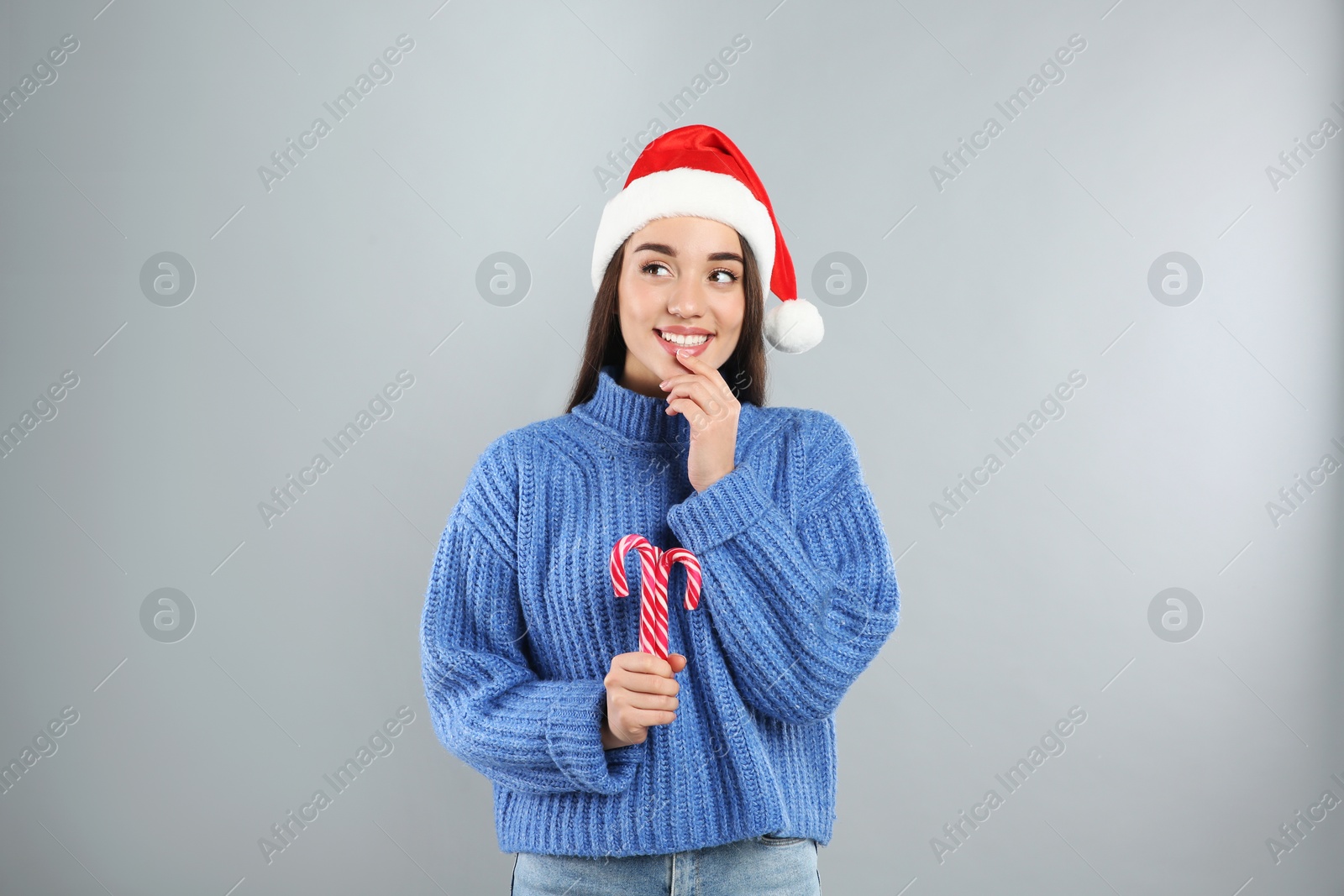 Young woman in blue sweater and Santa hat holding candy canes on grey background. Celebrating Christmas Photo of Young woman in blue sweater and Santa hat holding candy canes on grey background. Celebrating Christmas