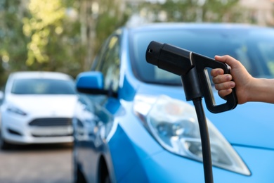 Woman holding power supply cable at electric vehicle charging station, closeup Photo of Woman holding power supply cable at electric vehicle charging station, closeup