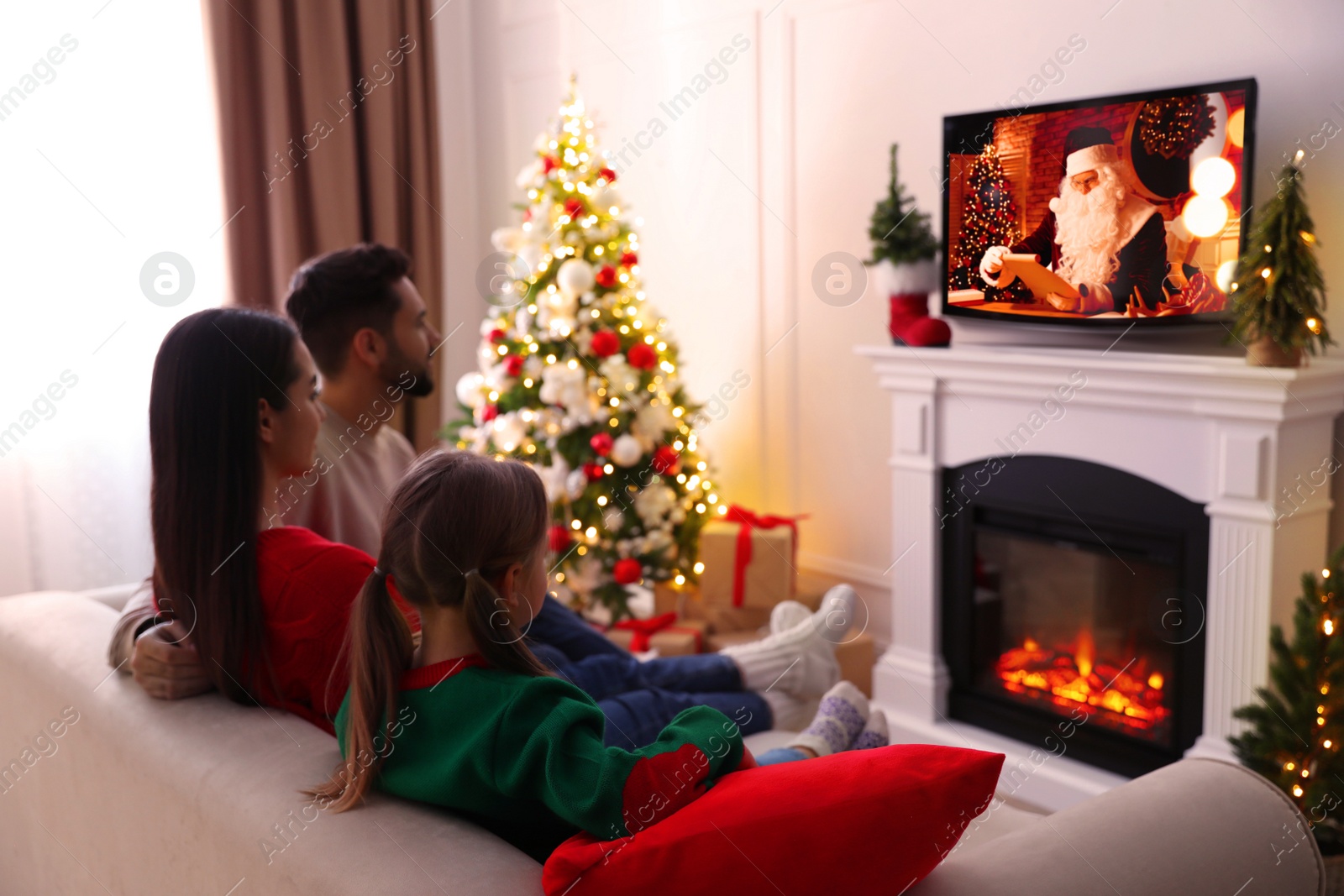 Family watching festive movie on TV in room decorated for Christmas Image of Family watching festive movie on TV in room decorated for Christmas
