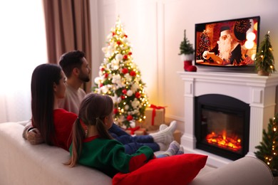 Family watching festive movie on TV in room decorated for Christmas Image of Family watching festive movie on TV in room decorated for Christmas