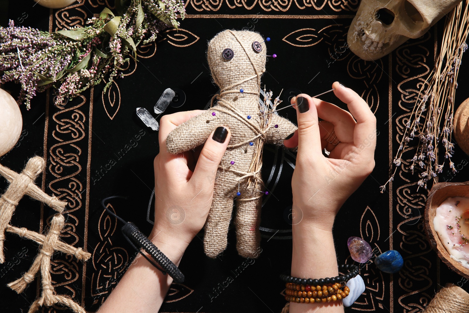 Woman stabbing voodoo doll with needle at table, closeup. Curse ceremony Photo of Woman stabbing voodoo doll with needle at table, closeup. Curse ceremony