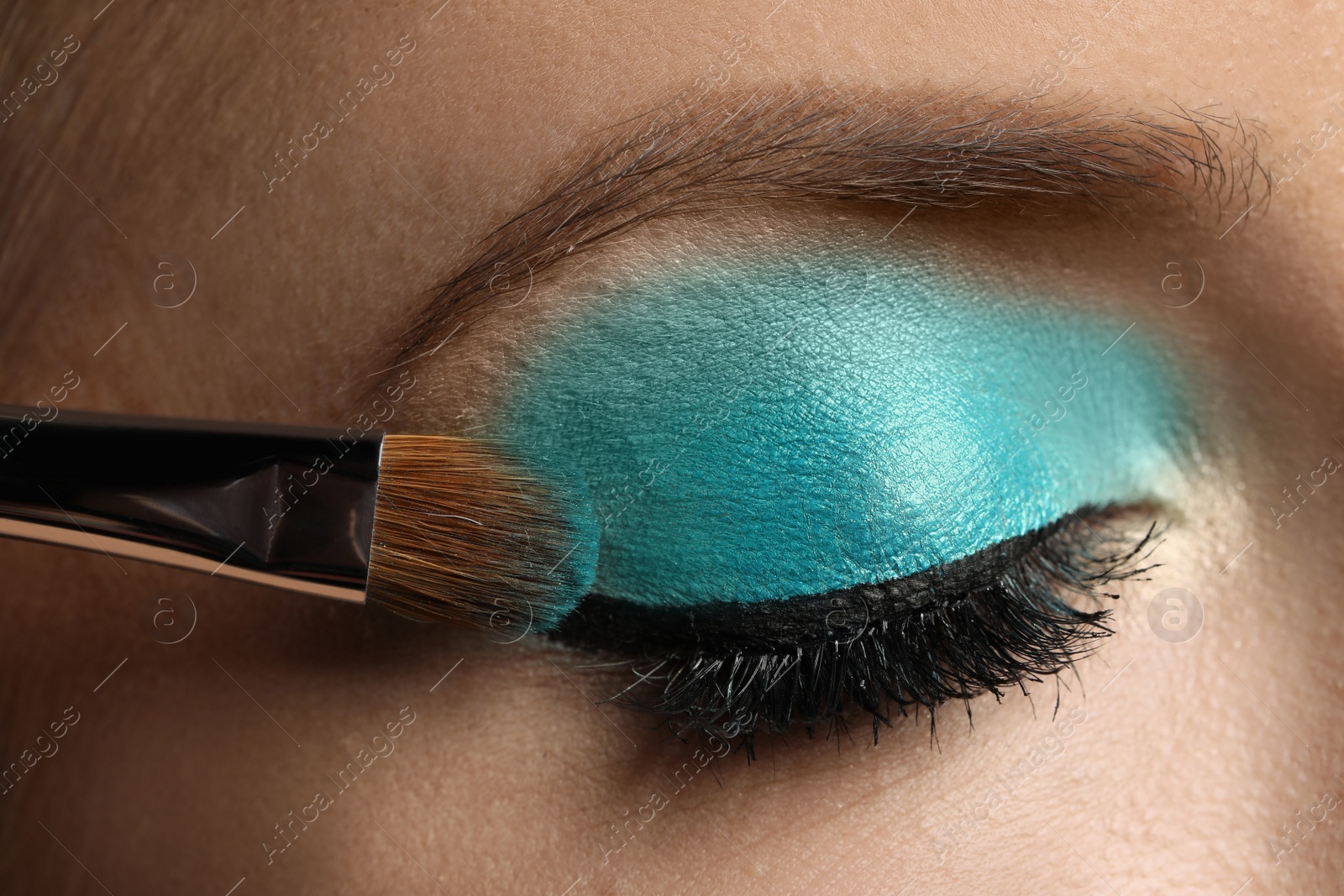 Photo of Applying cyan eye shadow onto woman's face, closeup. Beautiful evening makeup