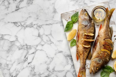 Photo of Tasty homemade roasted perches served on white marble table, top view and space for text. River fish