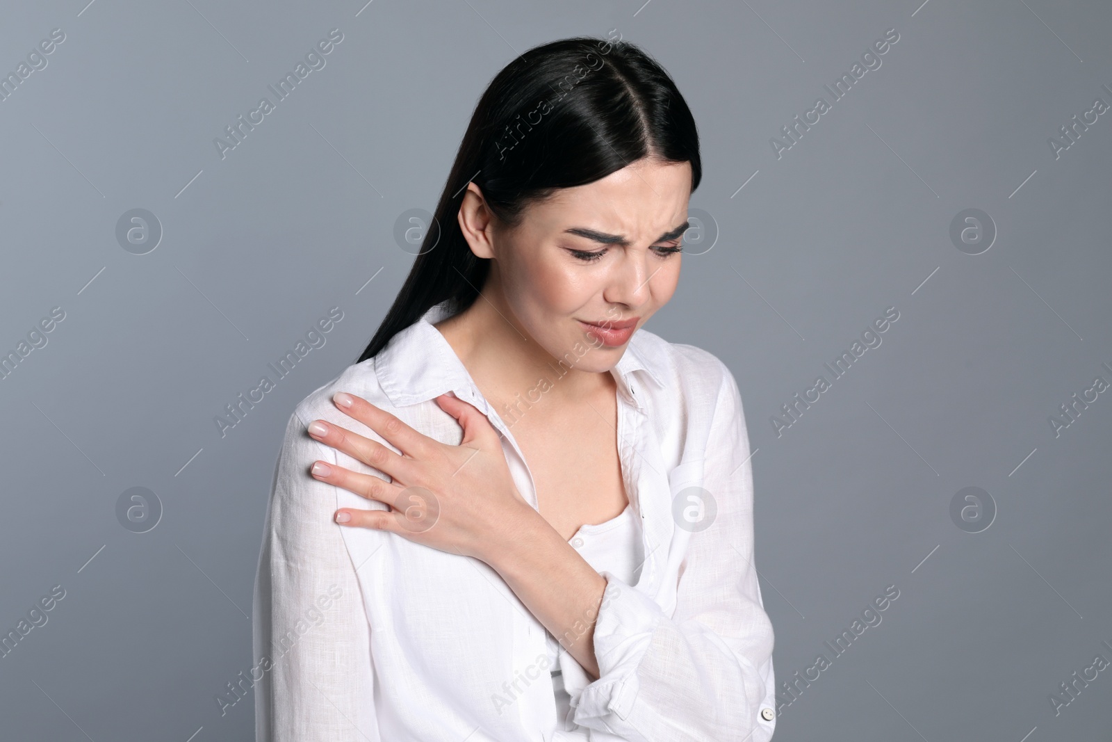 Woman suffering from shoulder pain on grey background Photo of Woman suffering from shoulder pain on grey background
