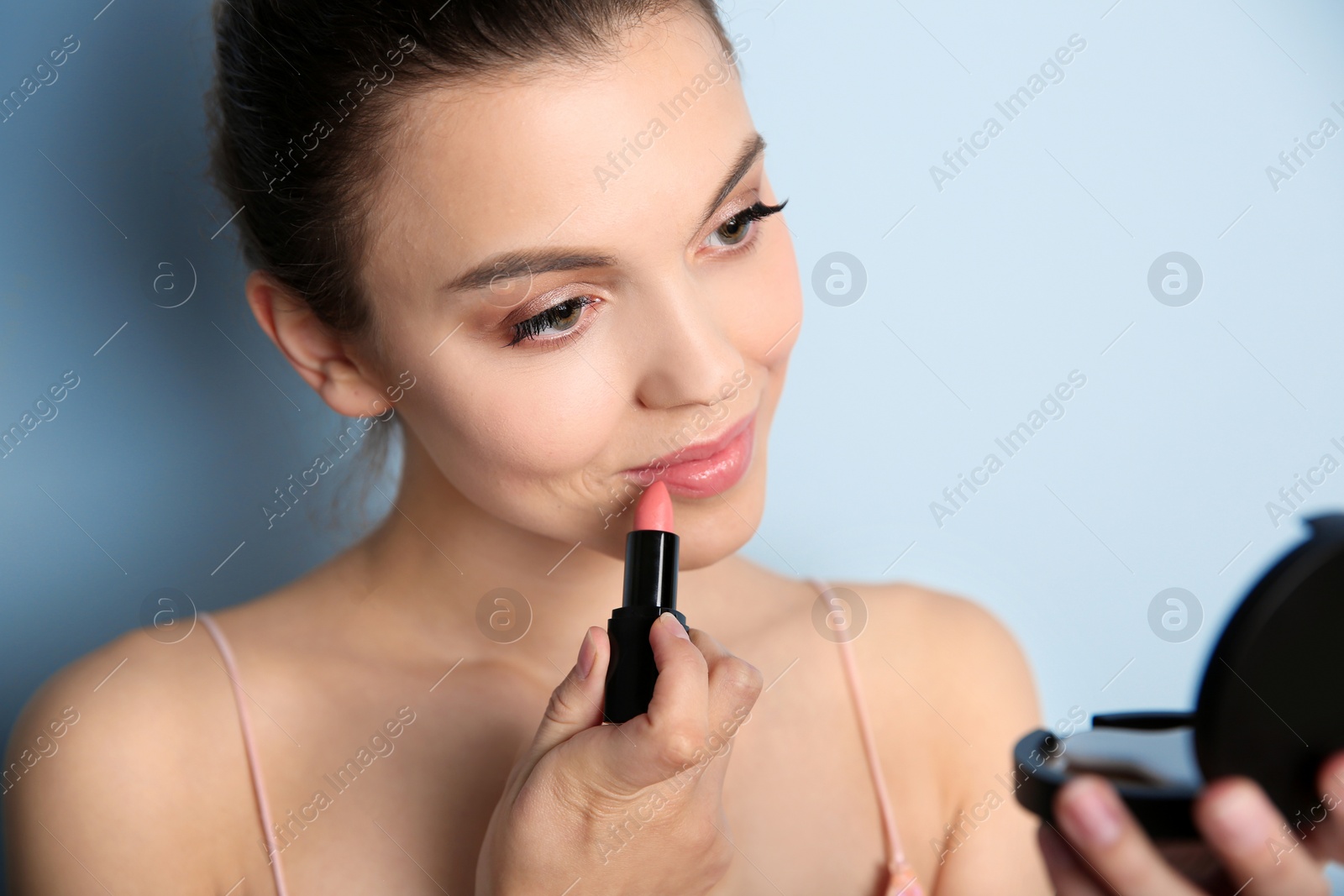 Young woman applying lipstick on color background. Professional makeup products Photo of Young woman applying lipstick on color background. Professional makeup products