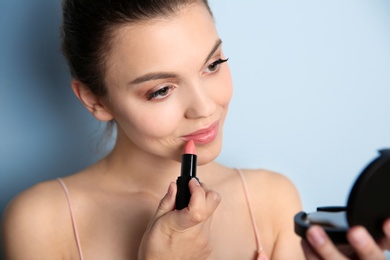 Photo of Young woman applying lipstick on color background. Professional makeup products