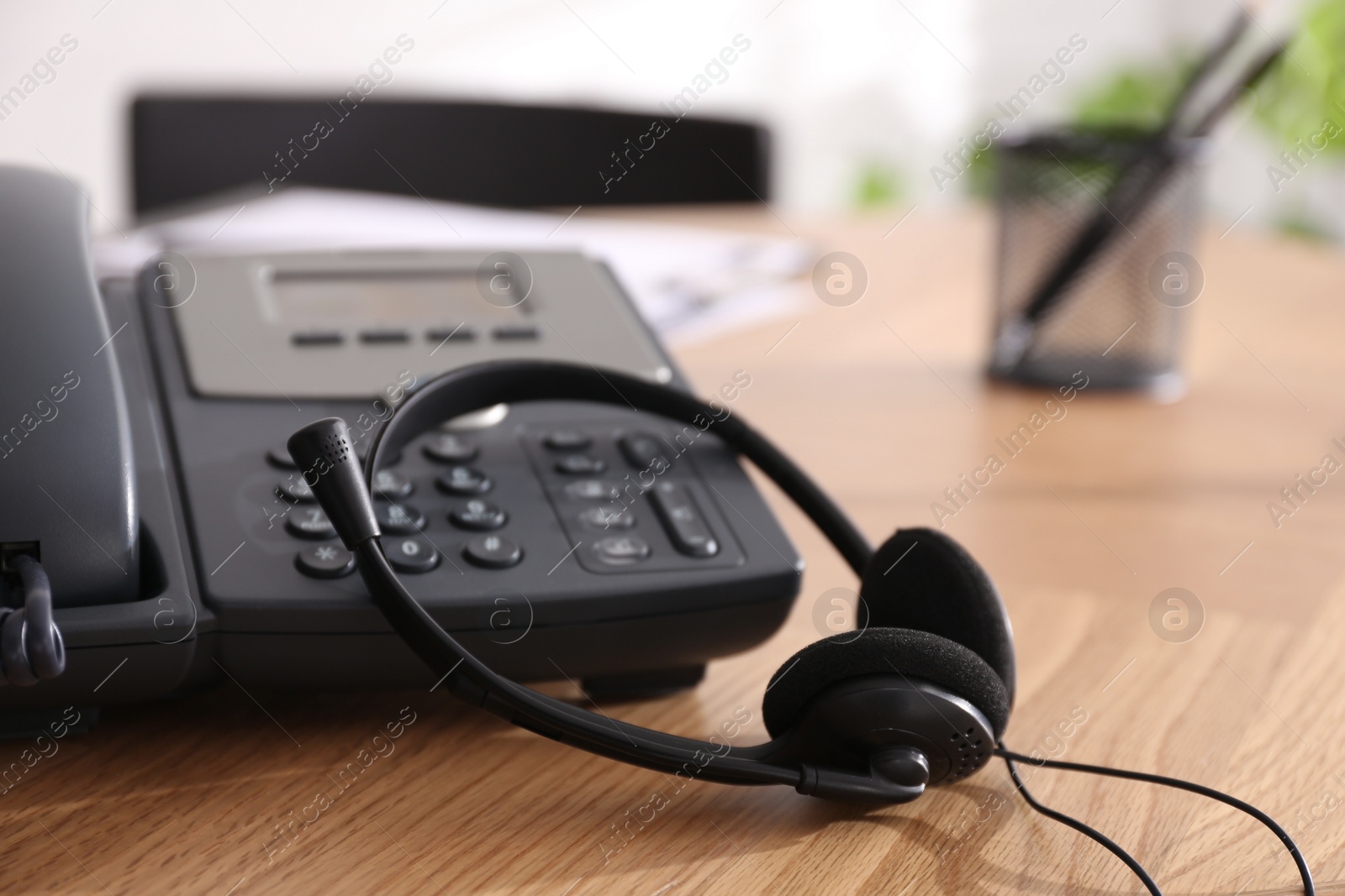 Desktop telephone and headset on wooden table in office, closeup. Hotline service Photo of Desktop telephone and headset on wooden table in office, closeup. Hotline service