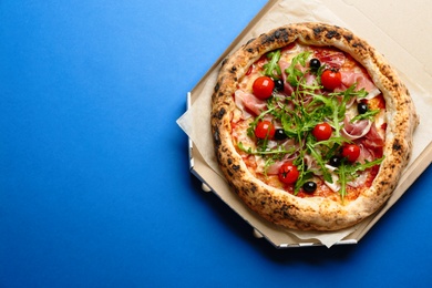 Tasty pizza with meat and arugula in cardboard box on blue background, top view. Space for text Photo of Tasty pizza with meat and arugula in cardboard box on blue background, top view. Space for text