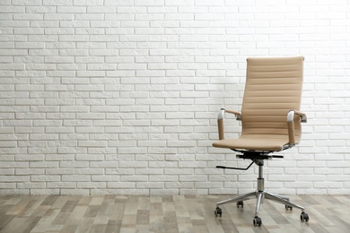 Comfortable office chair near white brick wall indoors. Space for text Photo of Comfortable office chair near white brick wall indoors. Space for text