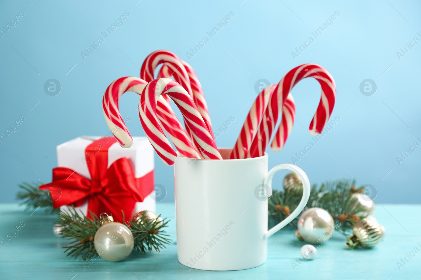 Many sweet candy canes in cup and Christmas decor on light blue wooden table Photo of Many sweet candy canes in cup and Christmas decor on light blue wooden table