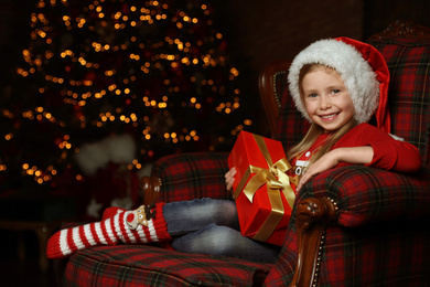 Cute little child with Christmas gift sitting in armchair at home Photo of Cute little child with Christmas gift sitting in armchair at home