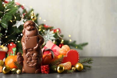 Composition with chocolate Santa Claus candies on grey table near Christmas tree, space for text Photo of Composition with chocolate Santa Claus candies on grey table near Christmas tree, space for text