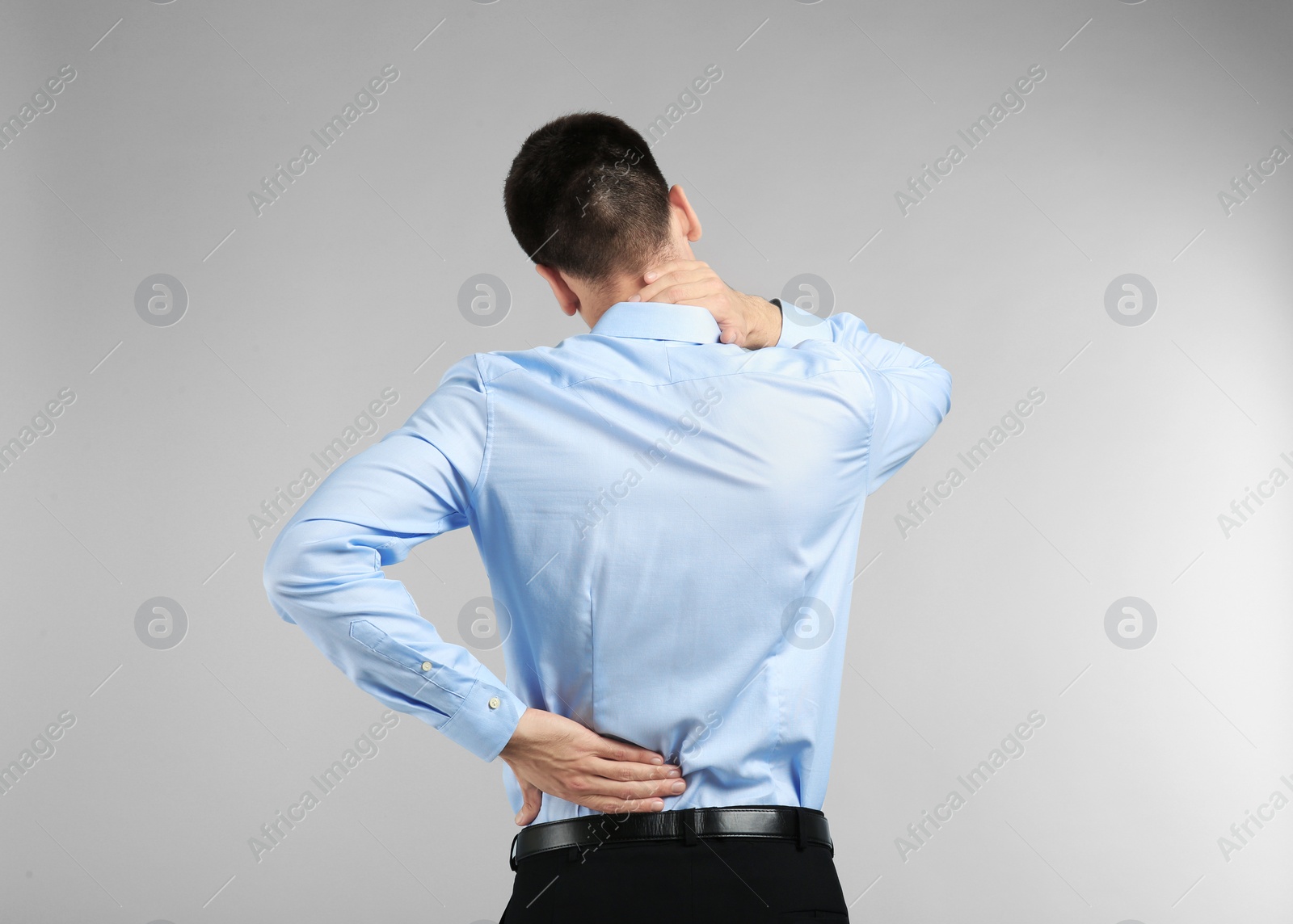 Young man suffering from back pain on light background Photo of Young man suffering from back pain on light background