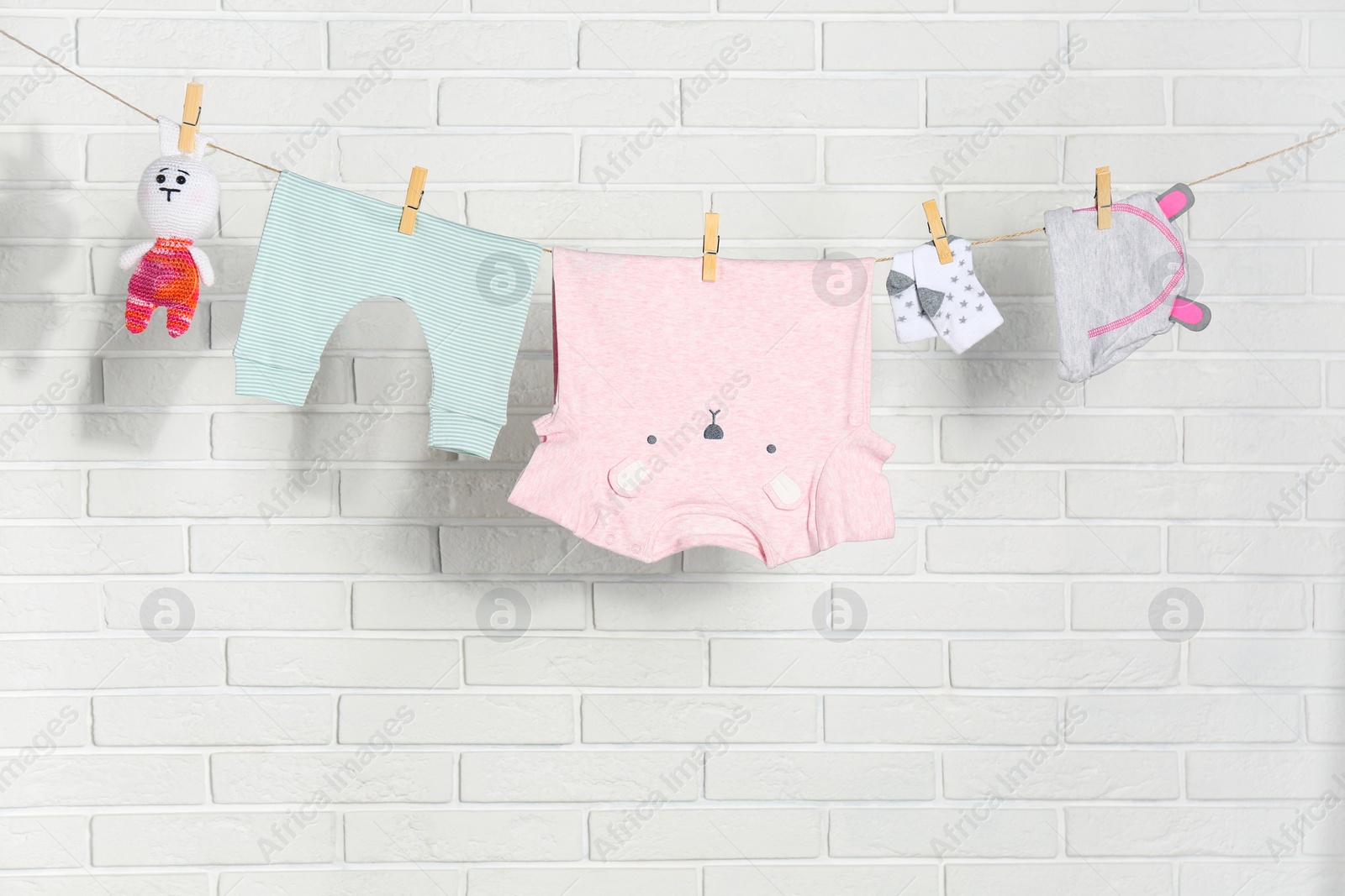 Baby clothes hanging on washing line near white brick wall Photo of Baby clothes hanging on washing line near white brick wall
