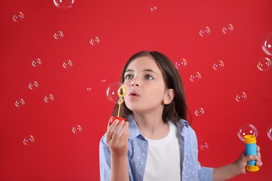 Photo of Little girl blowing soap bubbles on red background