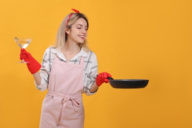 Young housewife with frying pan and glass of martini on yellow background. Space for text Photo of Young housewife with frying pan and glass of martini on yellow background. Space for text