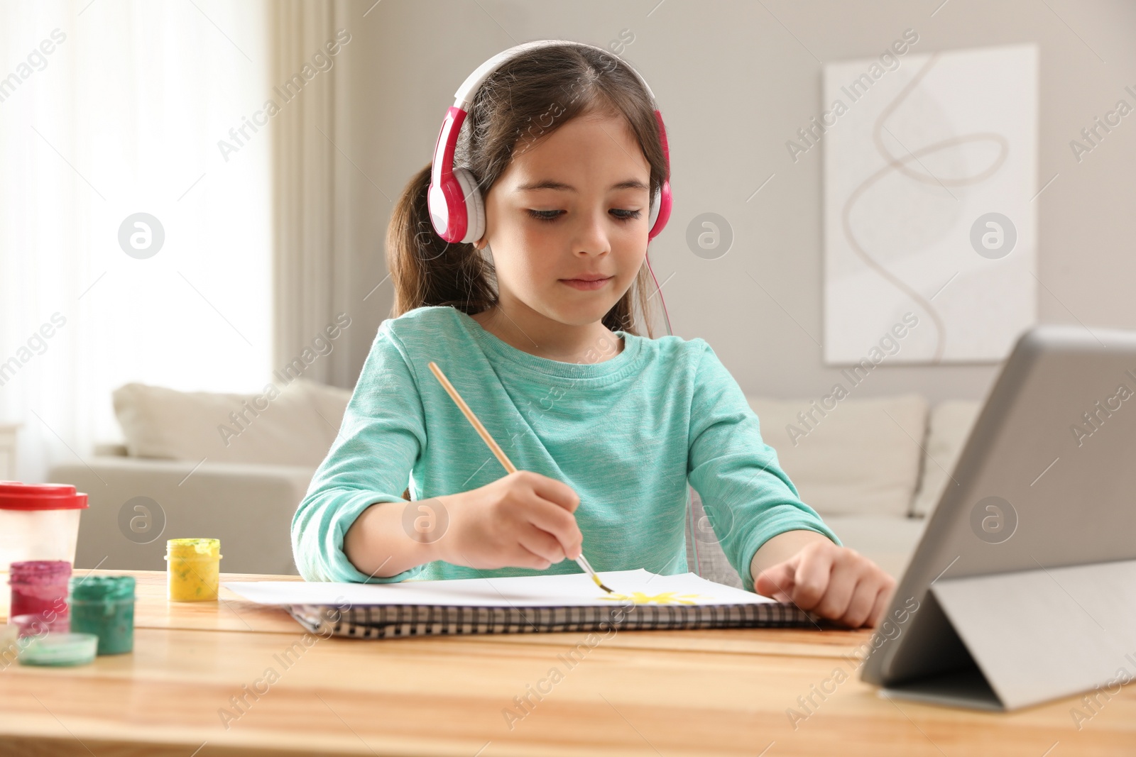 Little girl with headphones drawing on paper at online lesson indoors. Distance learning Photo of Little girl with headphones drawing on paper at online lesson indoors. Distance learning