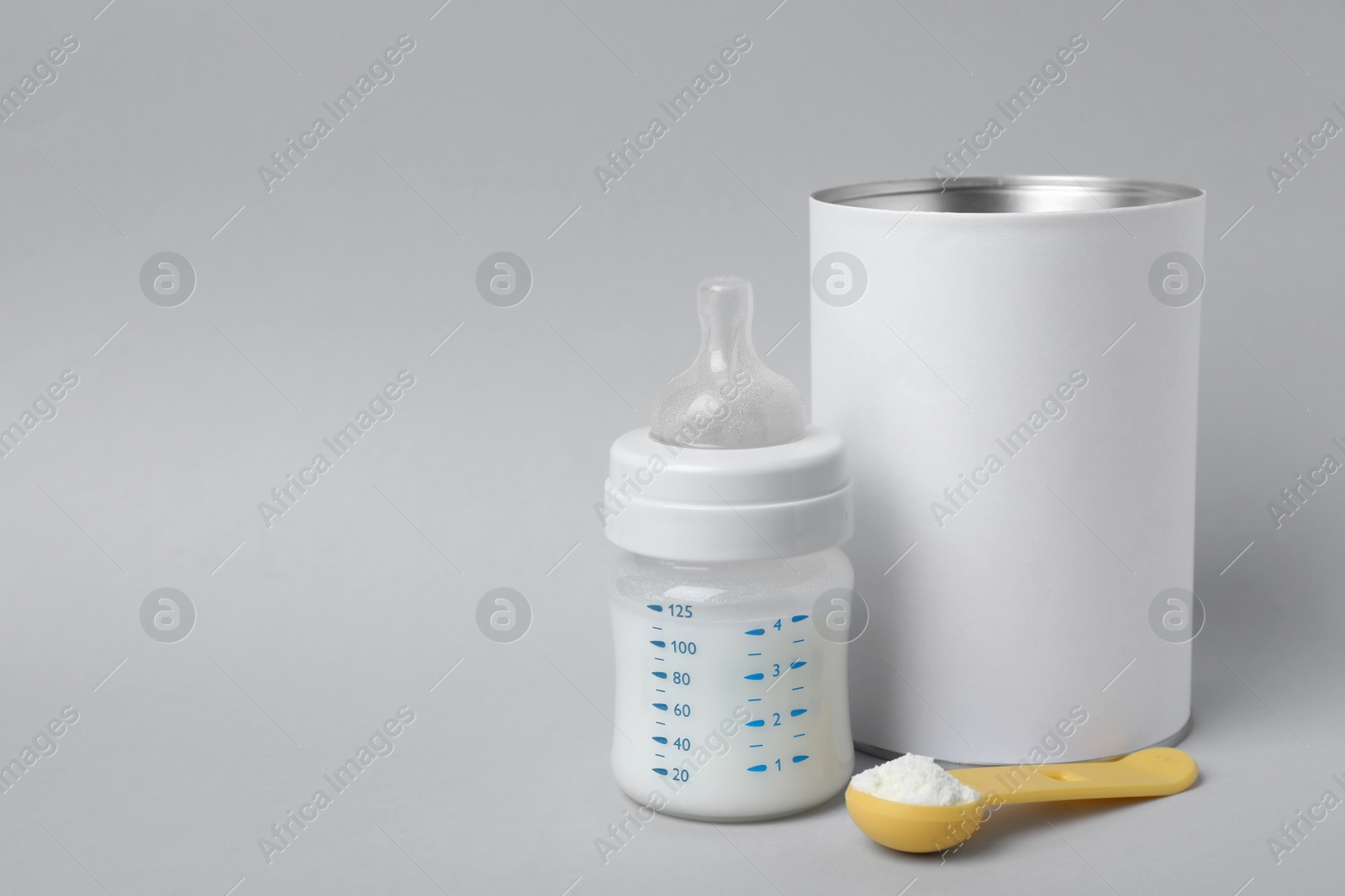 Blank can of powdered infant formula with scoop and feeding bottle on light grey background, space for text. Baby milk Photo of Blank can of powdered infant formula with scoop and feeding bottle on light grey background, space for text. Baby milk