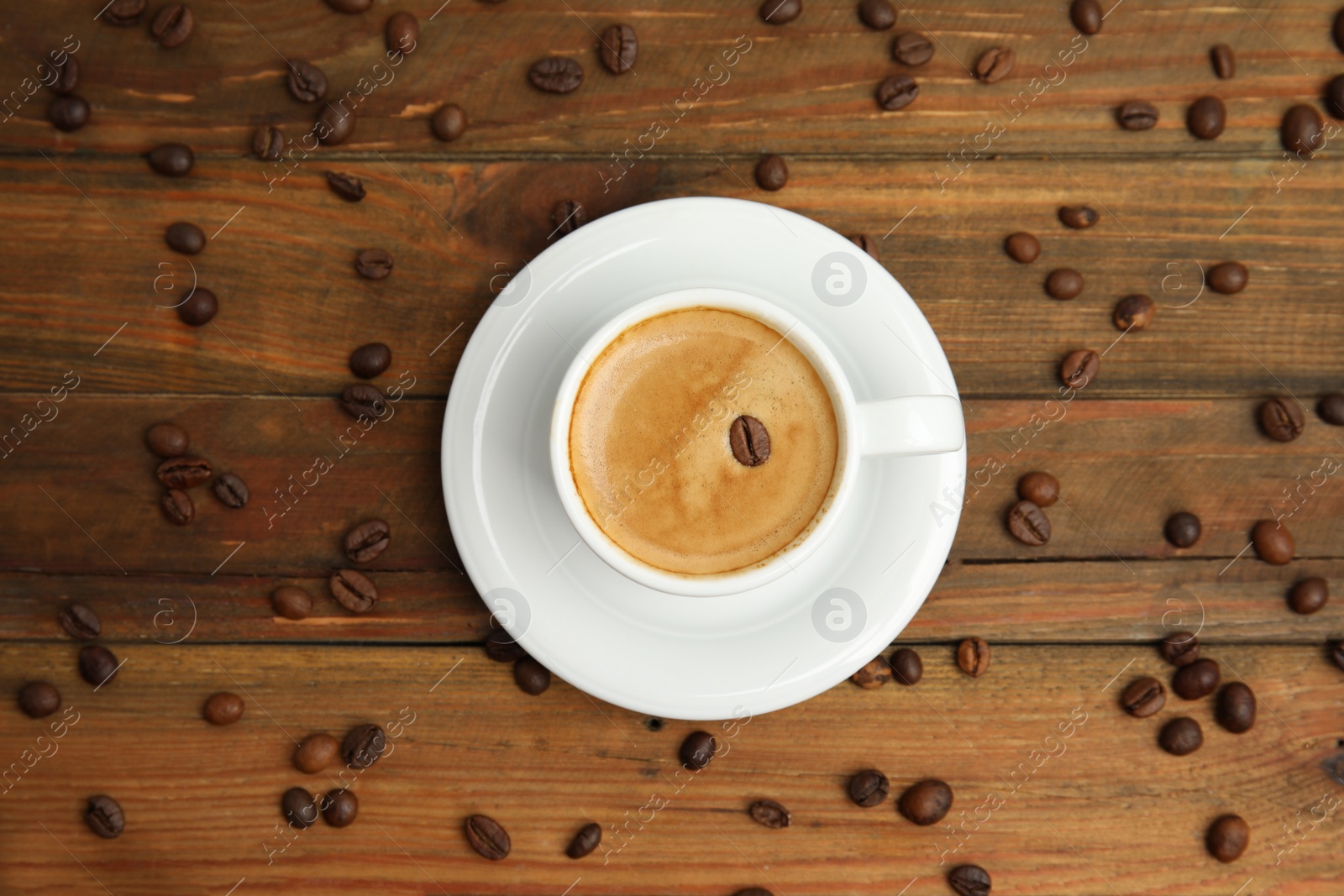Photo of Cup of tasty coffee and beans on wooden table, flat lay