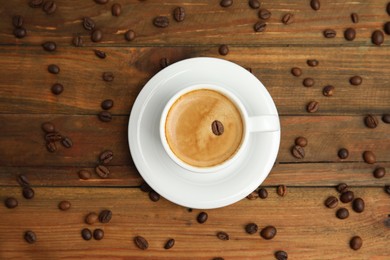 Photo of Cup of tasty coffee and beans on wooden table, flat lay