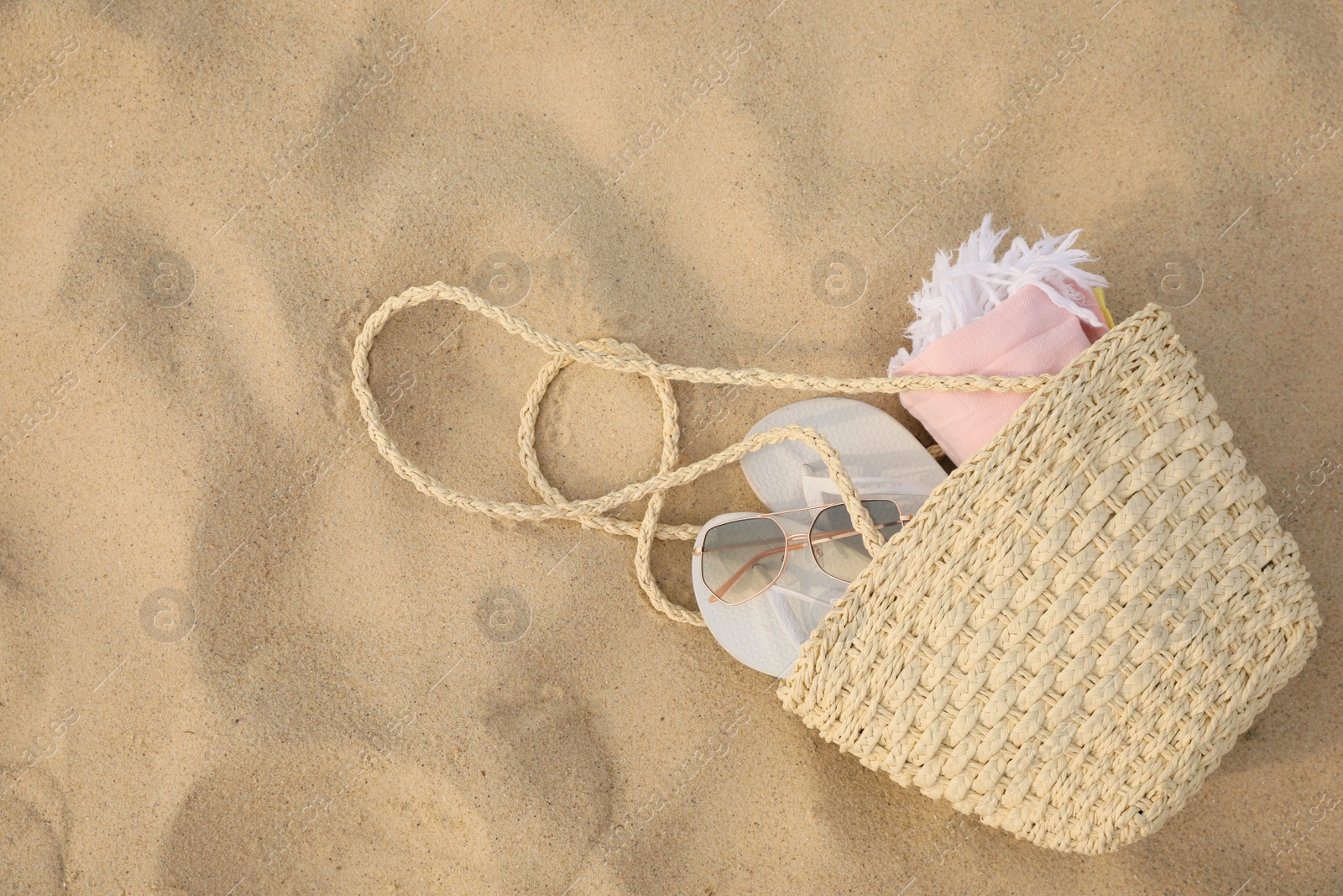 Beach bag with flip flops, towel and sunglasses on sand, top view. Space for text Photo of Beach bag with flip flops, towel and sunglasses on sand, top view. Space for text