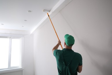 Man painting ceiling with roller in room, back view Photo of Man painting ceiling with roller in room, back view