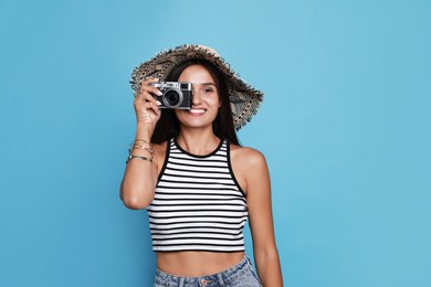 Beautiful young woman with straw hat and camera on light blue background Photo of Beautiful young woman with straw hat and camera on light blue background