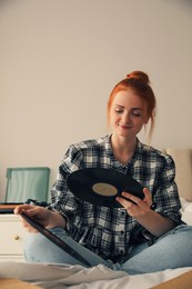 Young woman choosing vinyl disc to play music with turntable in bedroom Photo of Young woman choosing vinyl disc to play music with turntable in bedroom