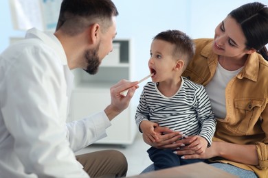 Photo of Mother and son visiting pediatrician in hospital. Doctor examining little boy