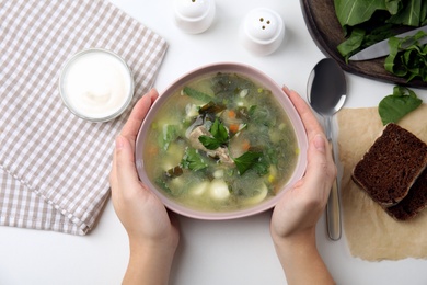 Photo of Woman eating delicious sorrel soup with meat and parsley at white table, top view