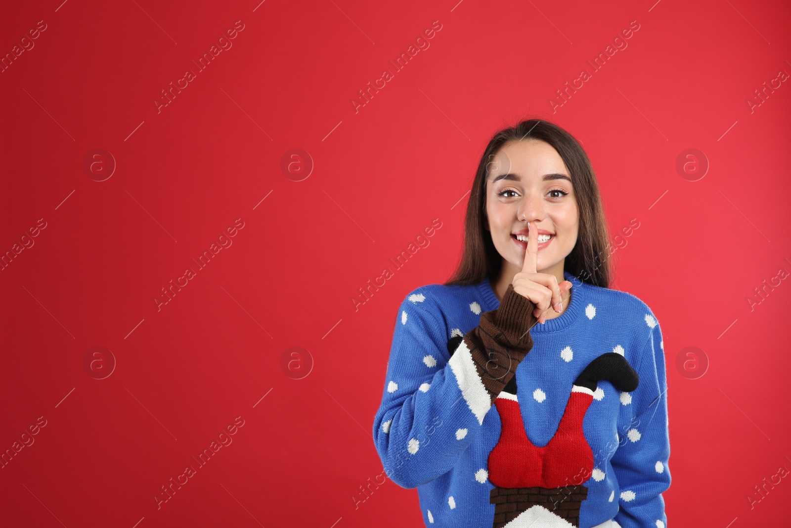 Young woman in Christmas sweater on red background, space for text Photo of Young woman in Christmas sweater on red background, space for text