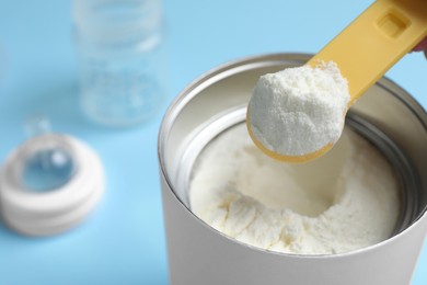 Scoop of powdered infant formula over can on light blue background, closeup. Baby milk Photo of Scoop of powdered infant formula over can on light blue background, closeup. Baby milk