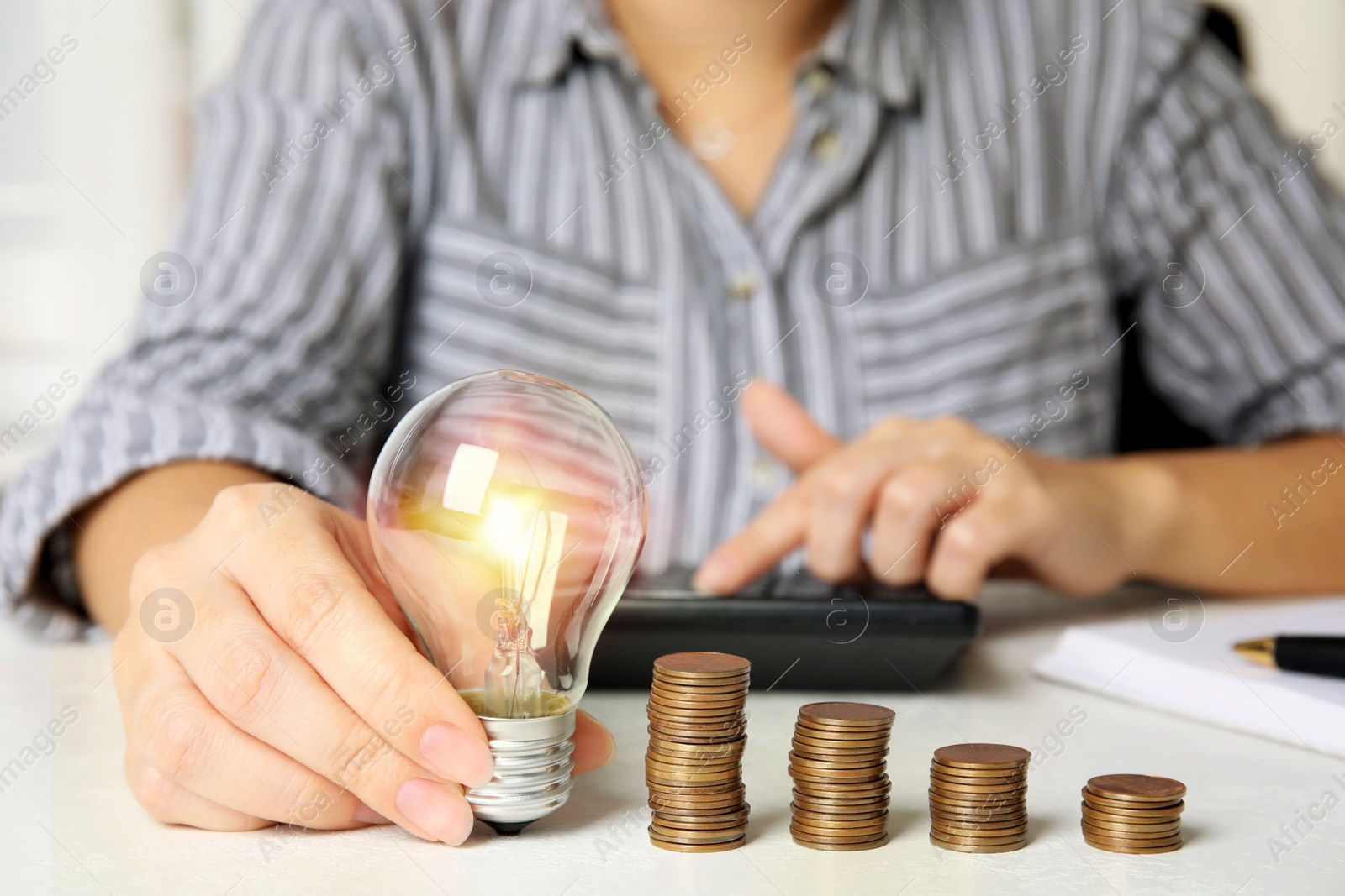 Woman with light bulb, calculator and coins at white table, closeup. Power saving Photo of Woman with light bulb, calculator and coins at white table, closeup. Power saving