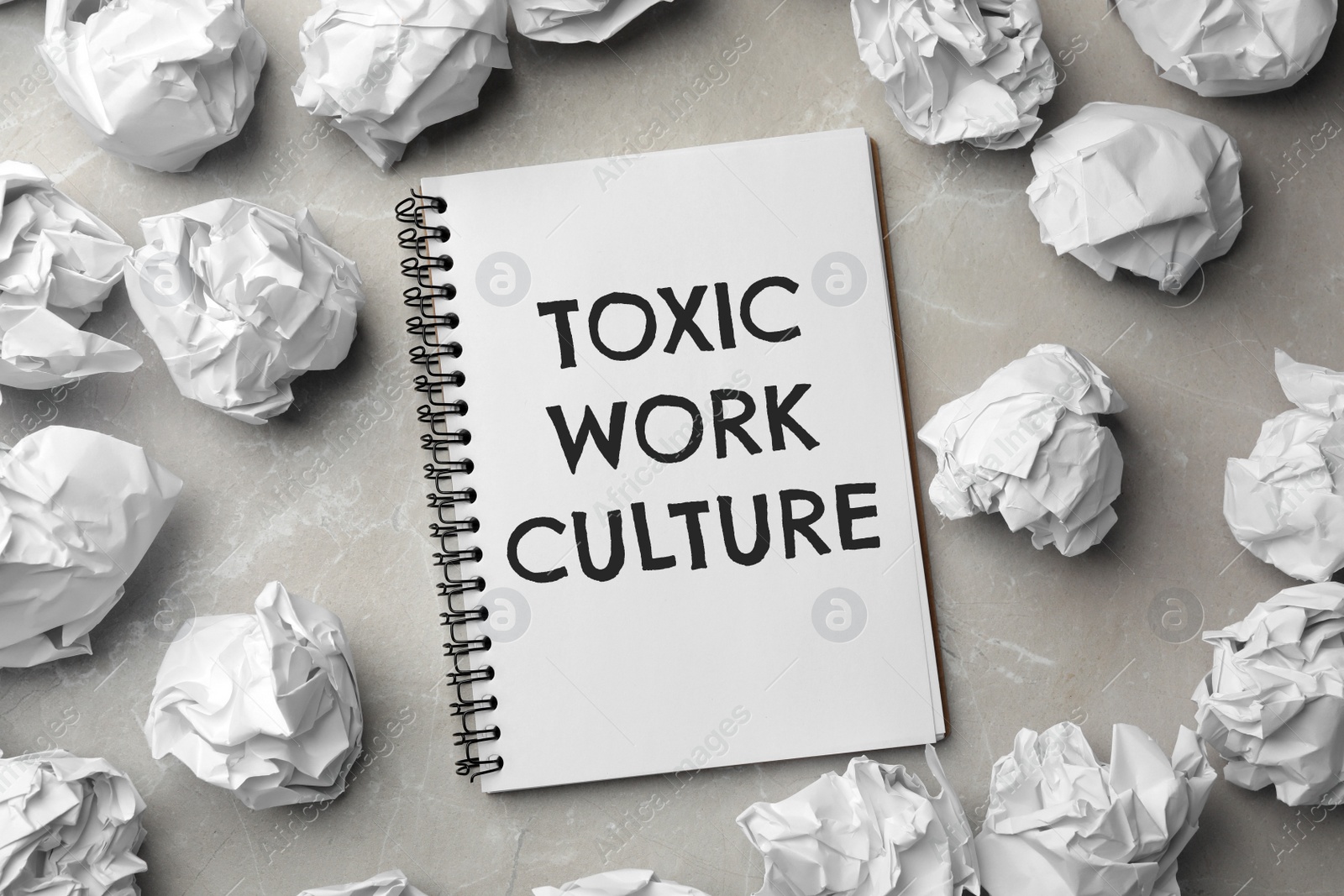 Notebook with text Toxic Work Culture and crumpled paper on grey marble table, flat lay Image of Notebook with text Toxic Work Culture and crumpled paper on grey marble table, flat lay