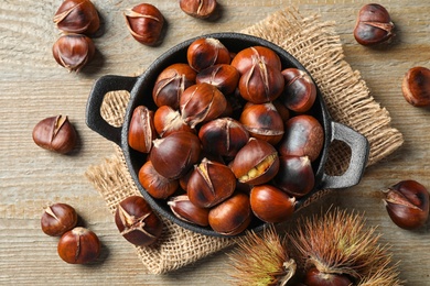 Tasty roasted edible chestnuts on wooden table, flat lay Photo of Tasty roasted edible chestnuts on wooden table, flat lay
