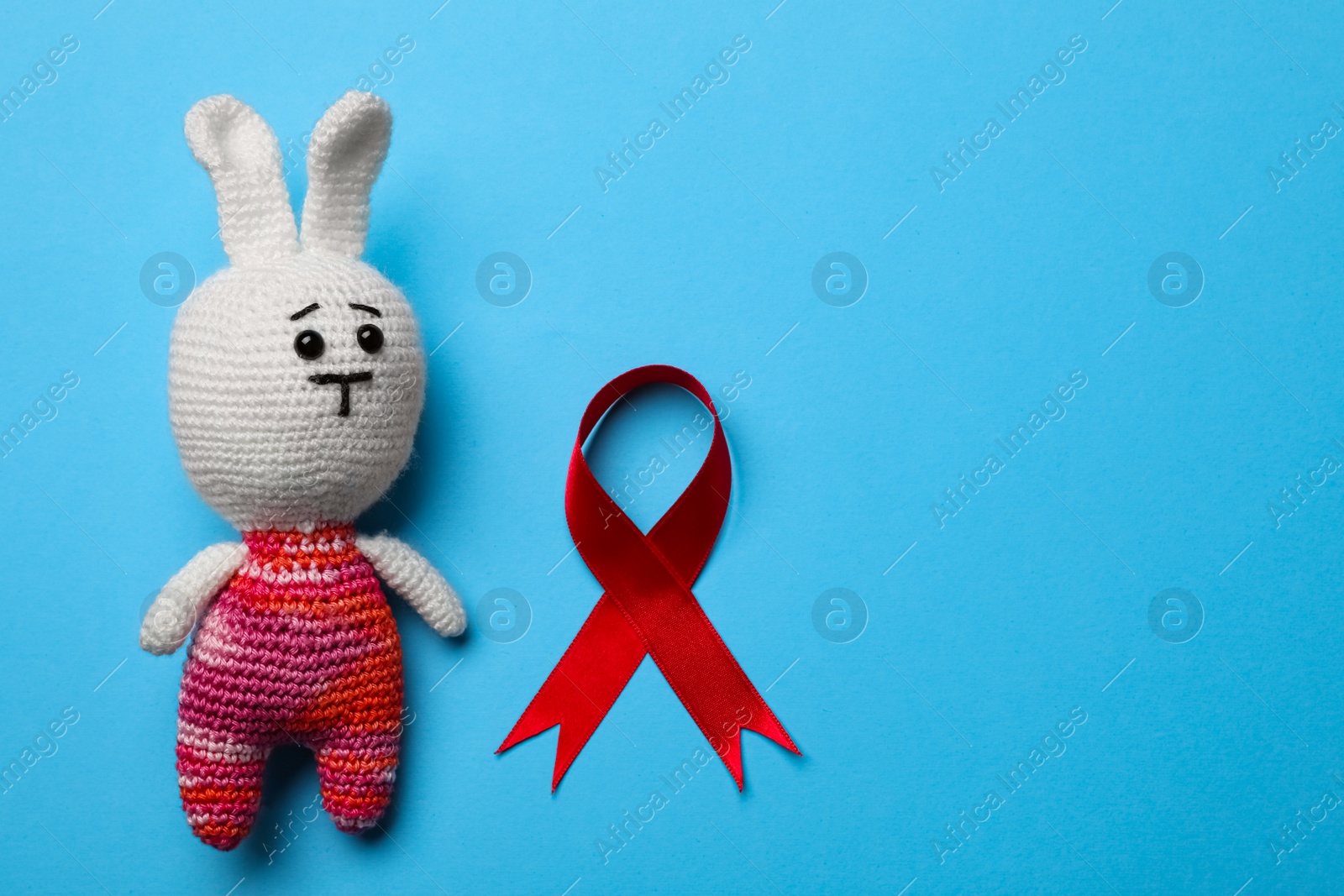 Cute knitted toy bunny and red ribbon on blue background, flat lay with space for text. AIDS disease awareness Photo of Cute knitted toy bunny and red ribbon on blue background, flat lay with space for text. AIDS disease awareness