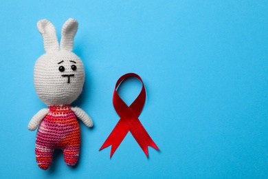 Cute knitted toy bunny and red ribbon on blue background, flat lay with space for text. AIDS disease awareness Photo of Cute knitted toy bunny and red ribbon on blue background, flat lay with space for text. AIDS disease awareness