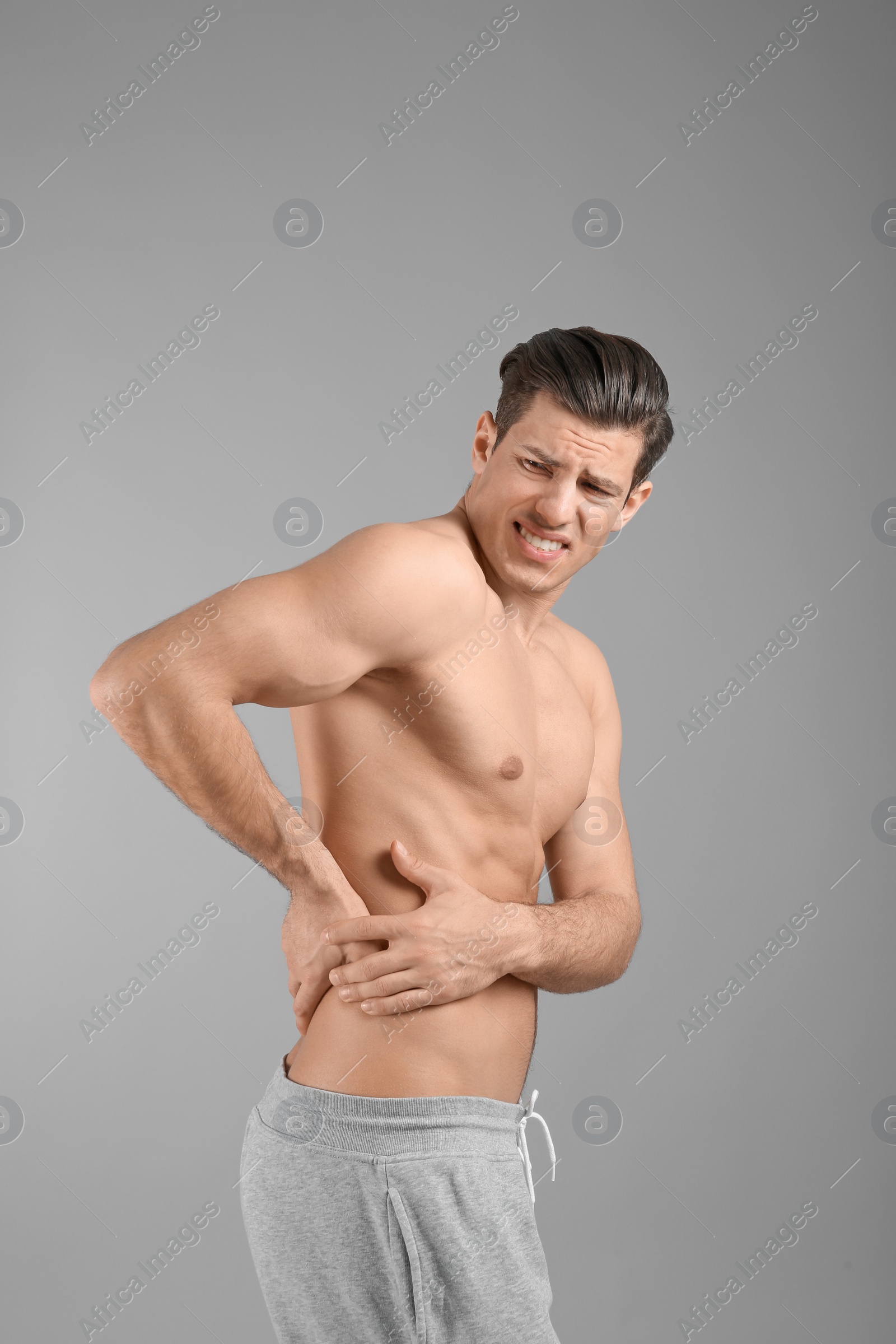 Young man suffering from flank pain on grey background Photo of Young man suffering from flank pain on grey background