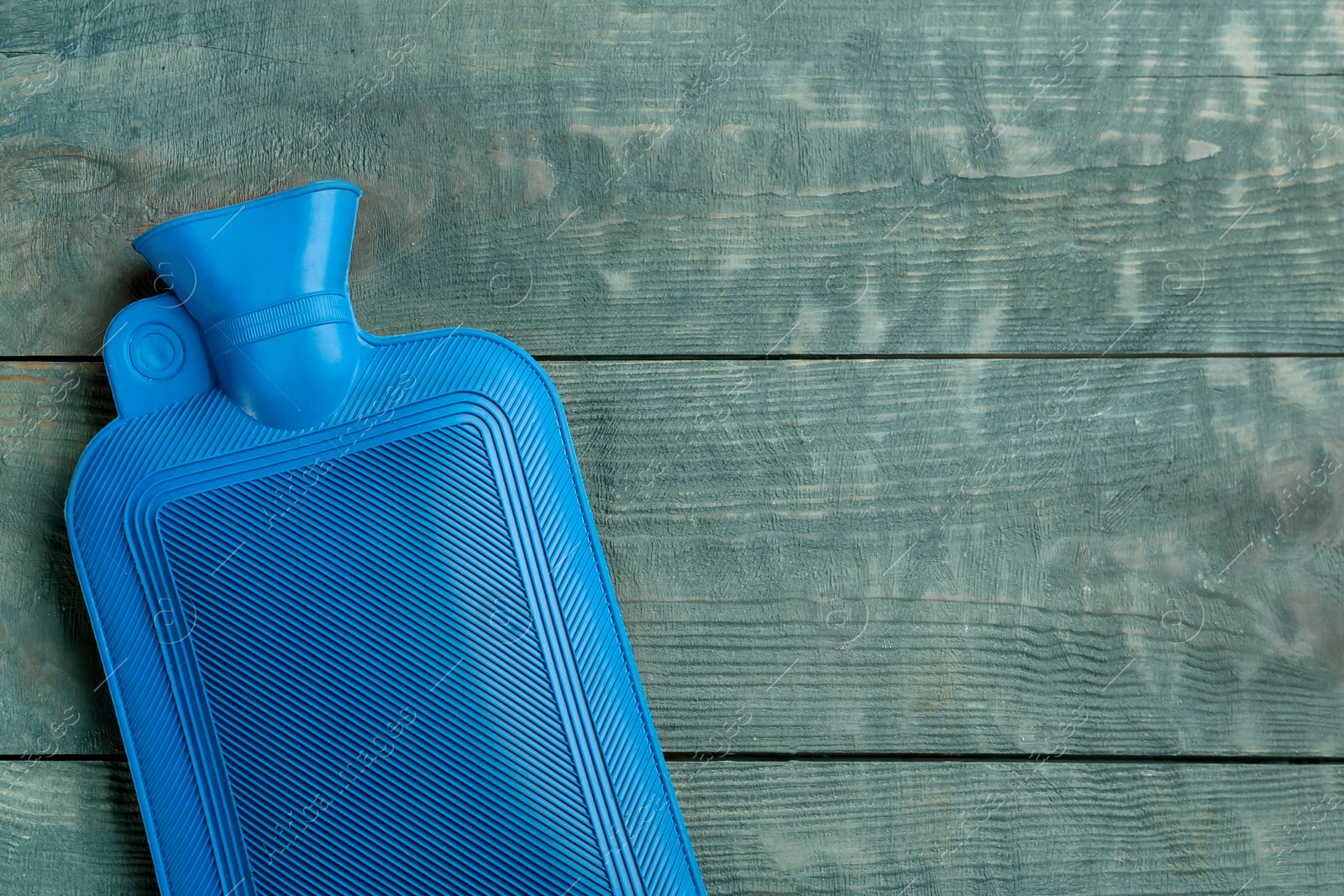 Photo of Rubber hot water bottle on light blue wooden background, top view. Space for text