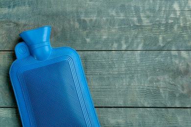 Photo of Rubber hot water bottle on light blue wooden background, top view. Space for text