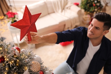 Man decorating Christmas tree in room, focus on star topper Photo of Man decorating Christmas tree in room, focus on star topper