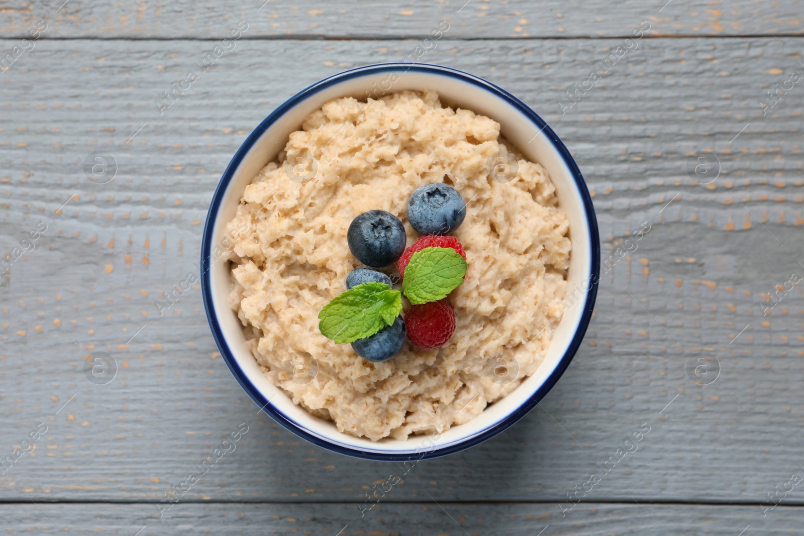 Tasty oatmeal porridge with berries on grey wooden table, top view Photo of Tasty oatmeal porridge with berries on grey wooden table, top view