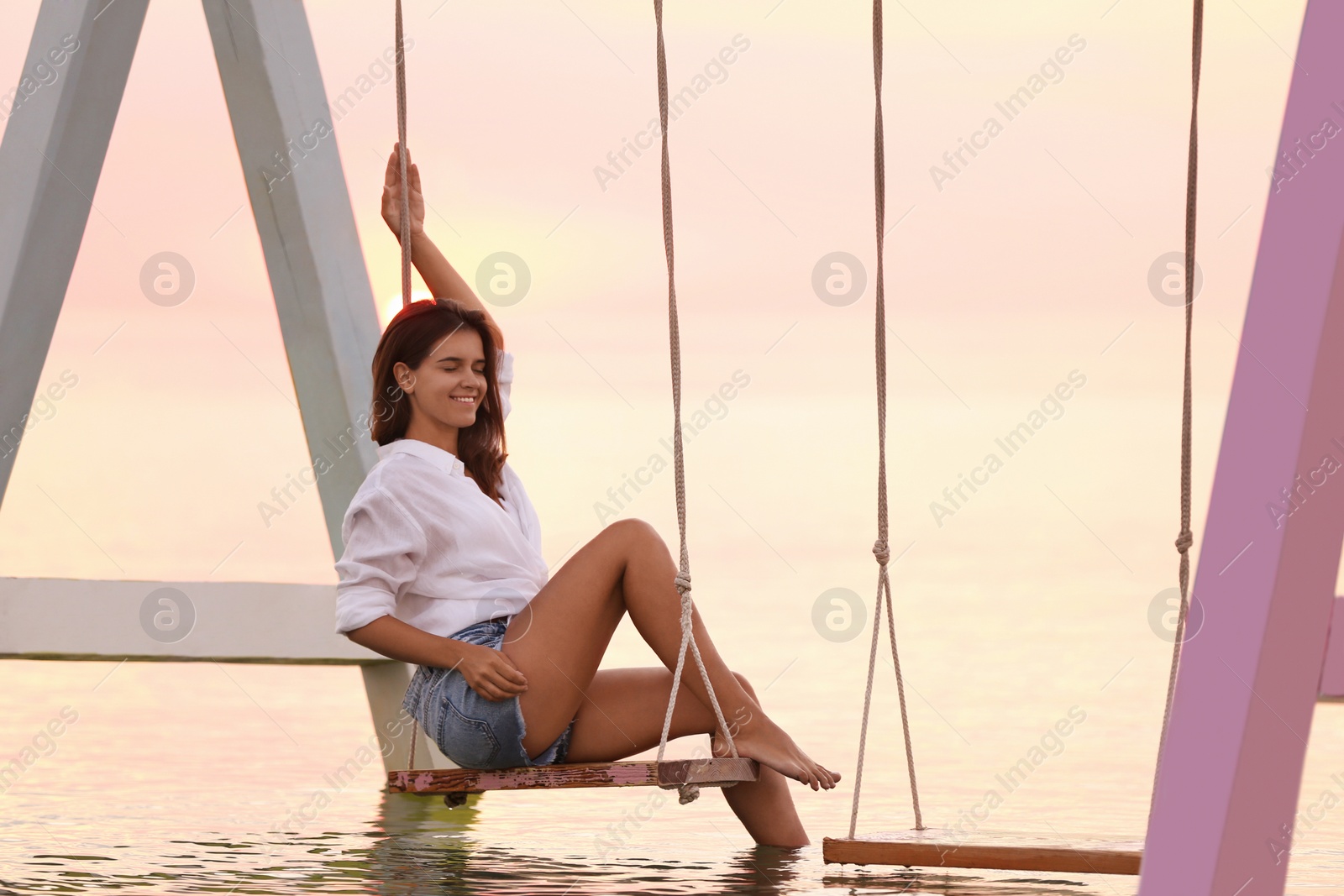 Young woman enjoying sunrise on swing over water Photo of Young woman enjoying sunrise on swing over water